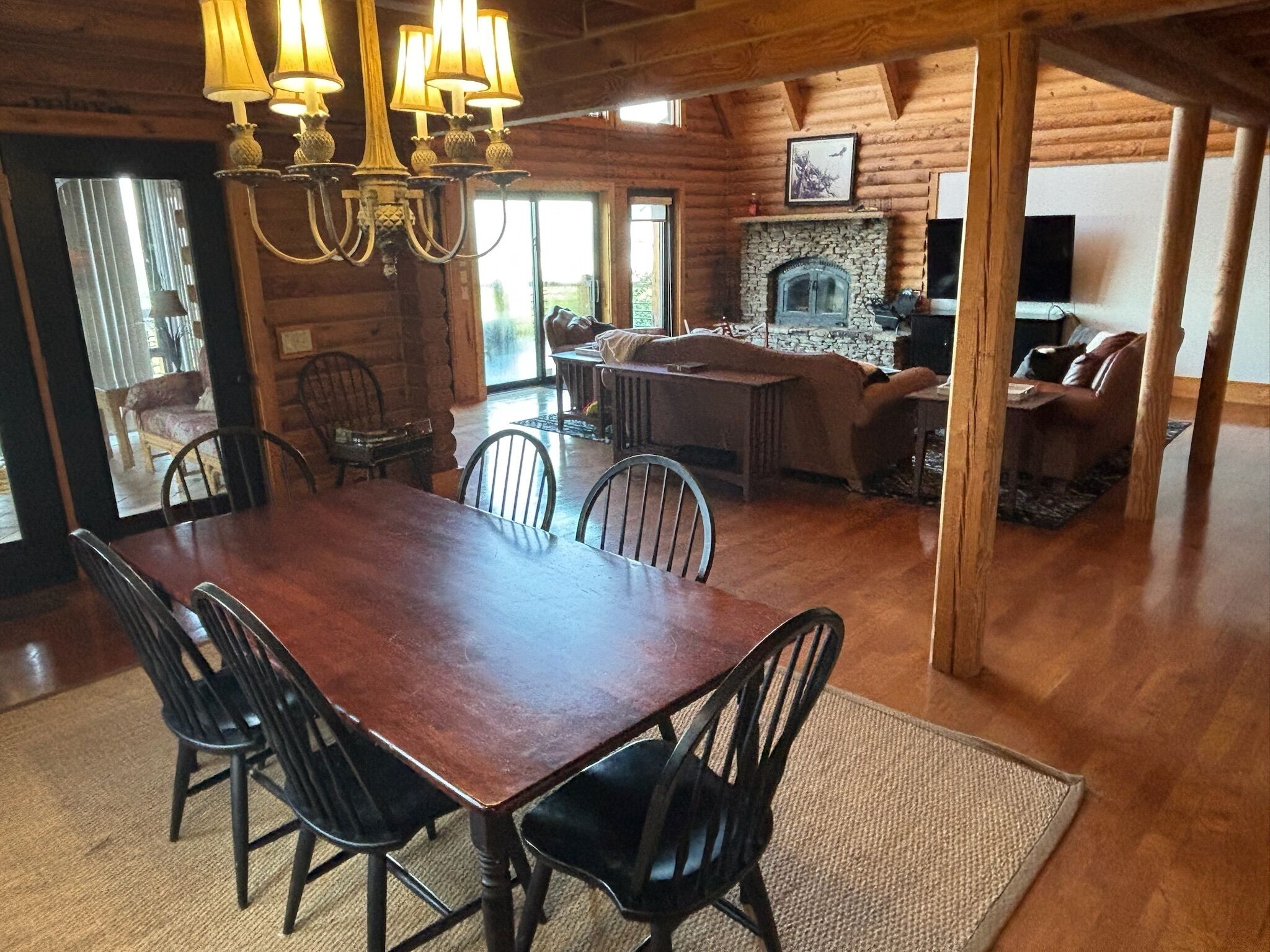 Un comedor amplio con una gran mesa y sillas de madera, una chimenea de piedra y una zona de estar acogedora con sofás y una televisión.