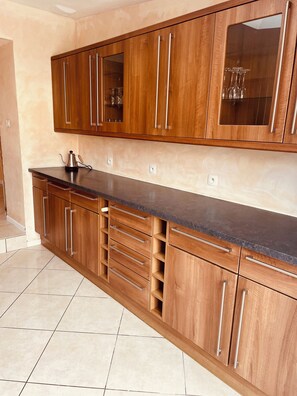 A kitchen with wooden cabinets, a black countertop, and a tiled floor. - Spacious Holiday Home for 9 with Private Garden (Outreau)