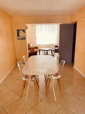 A dining area with a white table and chairs, a sofa, and a door leading to another room. - Spacious Holiday Home for 9 with Private Garden (Outreau)