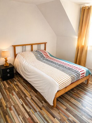 A bedroom with a sloped ceiling, a wooden bed frame, a patterned bedspread, a bedside table with a lamp, and a wooden floor. - Spacious Holiday Home for 9 with Private Garden (Outreau)