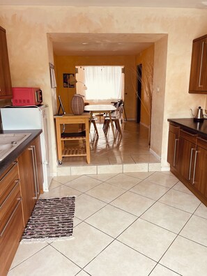 A kitchen with a dining area, wooden cabinets, a tiled floor, and a window with sheer curtains. - Spacious Holiday Home for 9 with Private Garden (Outreau)