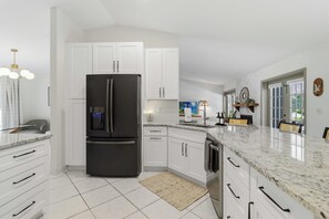 A modern kitchen with white cabinetry, a black refrigerator, and a granite countertop.