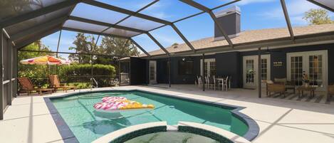 A swimming pool with a hot tub, surrounded by a covered patio area with outdoor furniture.