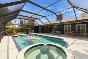 A swimming pool with a hot tub, surrounded by a covered patio area with outdoor furniture.