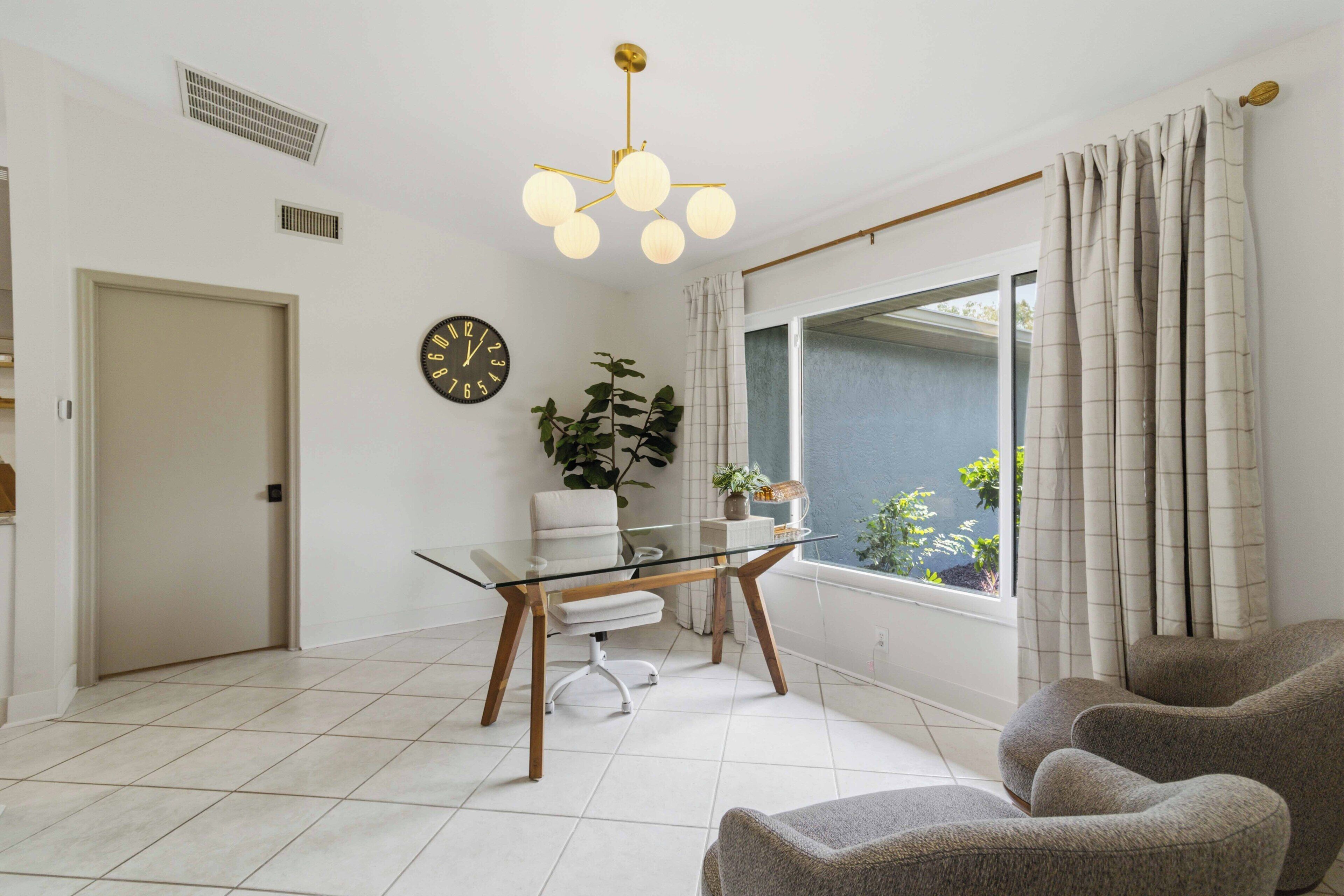 Un salon moderne avec une table en verre, un canapé, une plante en pot et une vue sur l’extérieur à travers une fenêtre avec des rideaux.