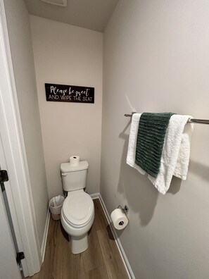 Ein kleines Badezimmer mit Toilette, Toilettenpapier, einem Mülleimer und einem Handtuchhalter mit einem grünen Handtuch.