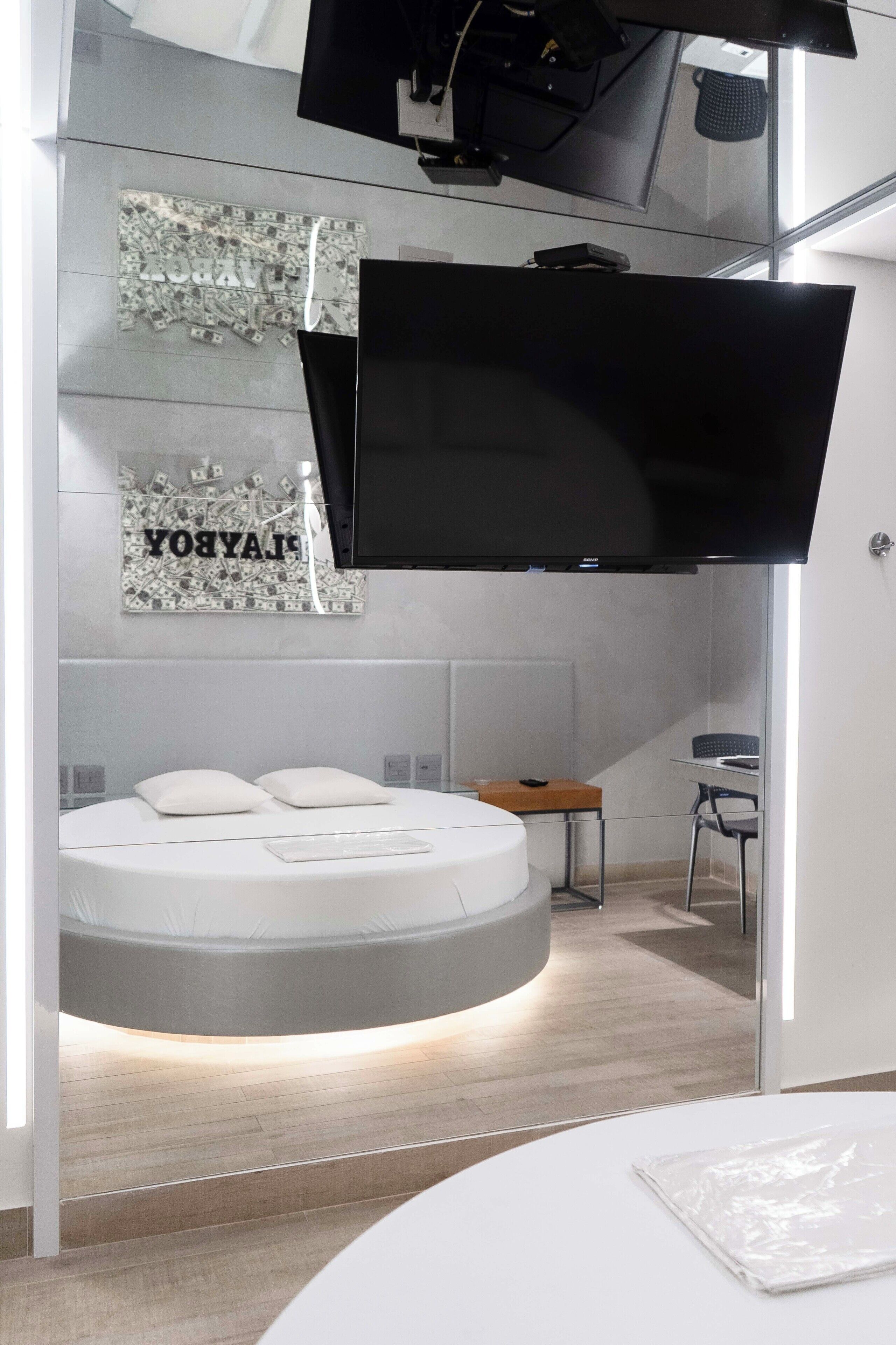 Quarto de hotel moderno com uma cama, uma televisão de tela plana na parede e uma pequena mesa.