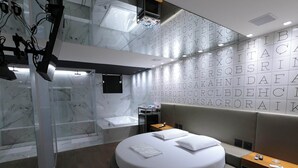 A modern hotel room with a circular bed, a glass-enclosed shower, and a wall with alphabet letters. - Motel Cavalo Branco (Belo Horizonte)