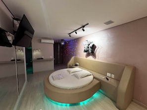 A modern bedroom with a circular bed, bedside controls, and a wall-mounted TV.