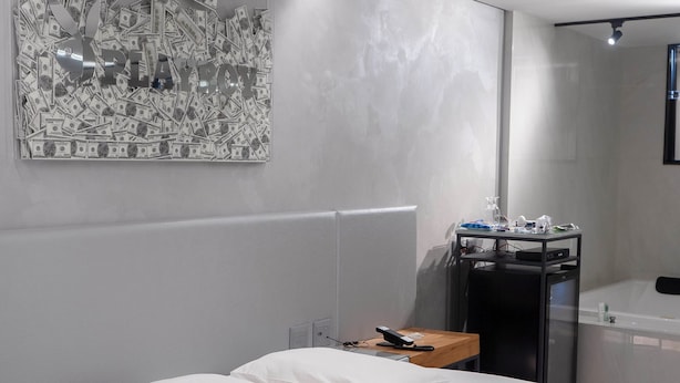 Un dormitorio moderno con una cama redonda, una mesita de noche de madera, un escritorio con computadora y un baño con bañera.