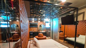 A modern hotel room with a large bed, a bathroom with a glass partition, and a seating area with a tufted headboard. - Motel Cavalo Branco (Belo Horizonte)