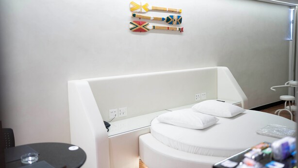 A modern hotel room with a white bed, a small table, and a wall-mounted TV. - Motel Cavalo Branco (Belo Horizonte)