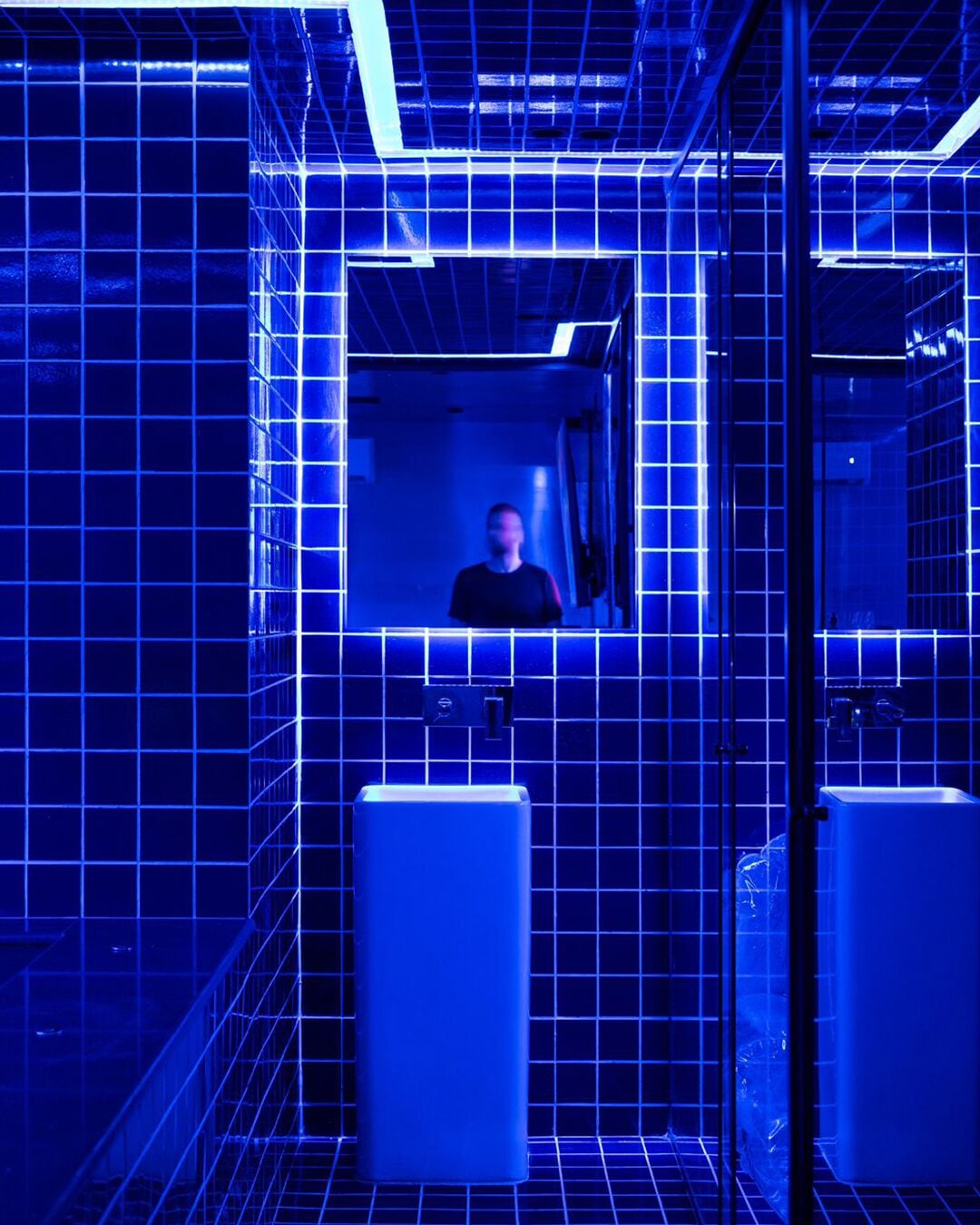A restroom with blue-tiled walls, a mirror, and two sinks.