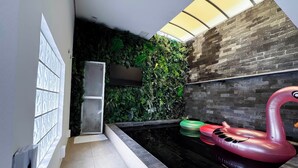 A modern indoor pool area with a glass wall, a brick wall, and a green wall with plants. There are inflatable flamingos and a white inflatable swan. - Motel Cavalo Branco (Belo Horizonte)