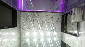 Un baño con paredes de azulejos blancos, un secador de manos y un espejo.