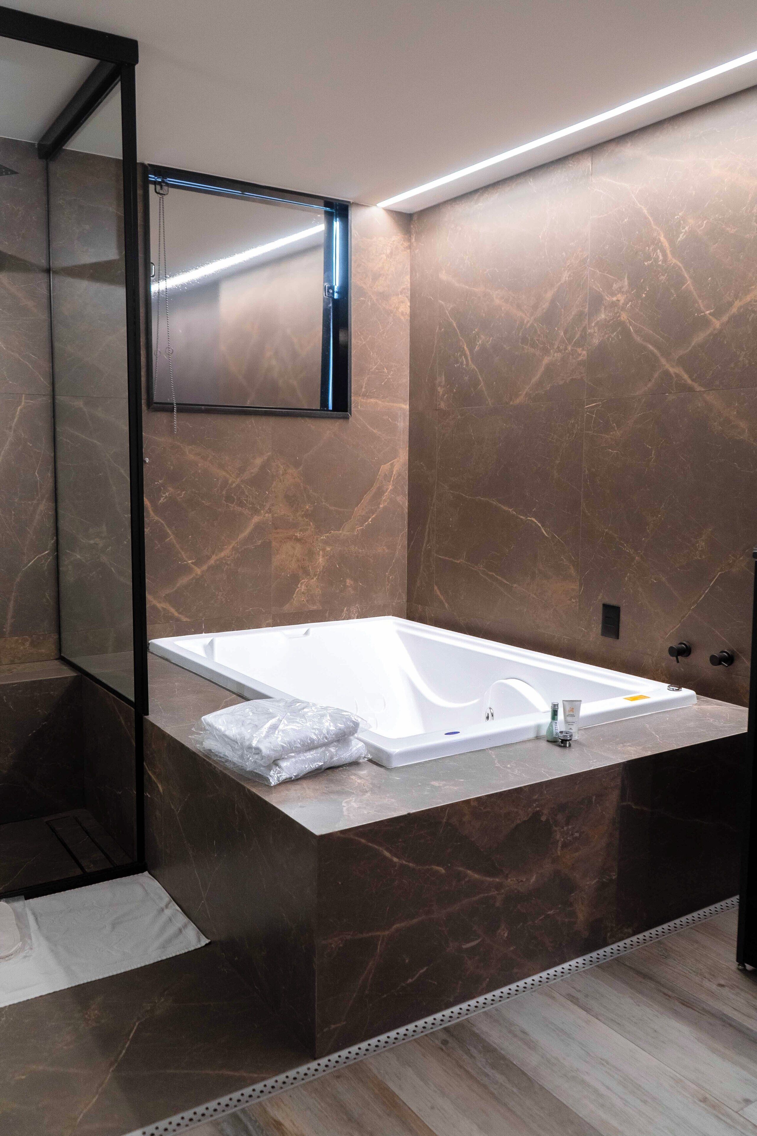 Un baño moderno con una bañera grande, un espejo y paredes de mármol.