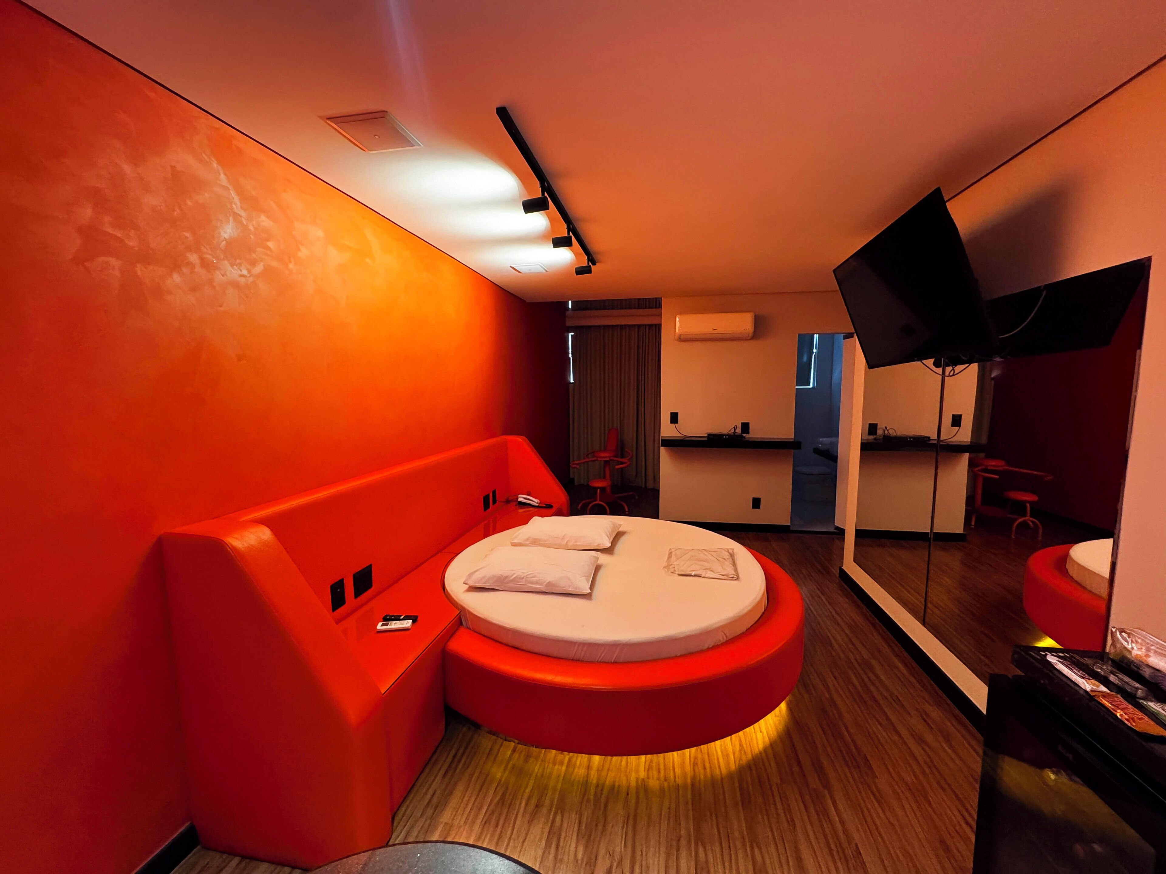 Un dormitorio moderno con cama redonda, paredes de acento rojas, televisor de pantalla plana y una pequeña kitchenette.