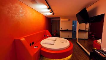 Un dormitorio moderno con cama redonda, paredes de acento rojas, televisor de pantalla plana y una pequeña kitchenette.
