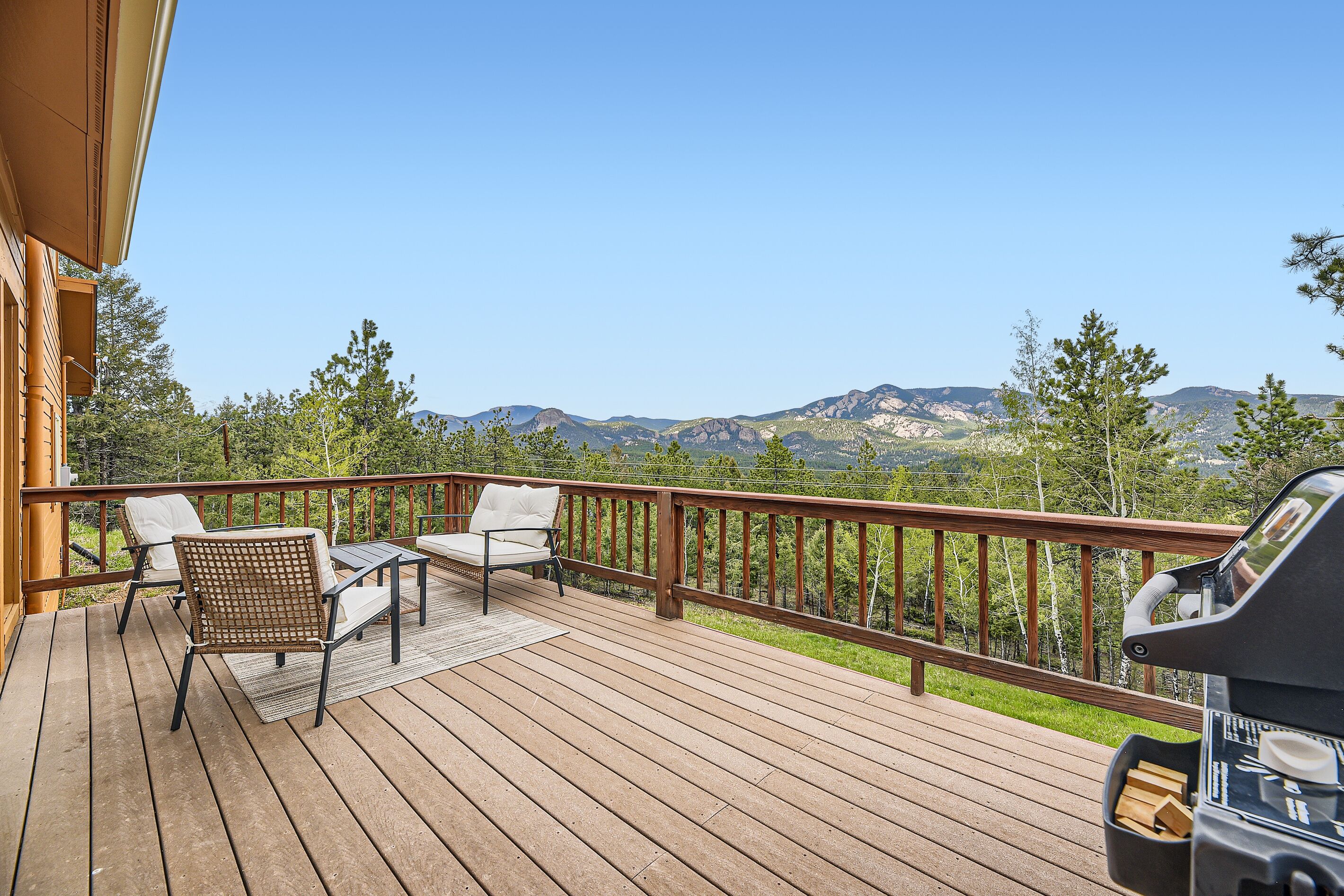A wooden deck with outdoor furniture and a grill, overlooking a mountainous landscape.