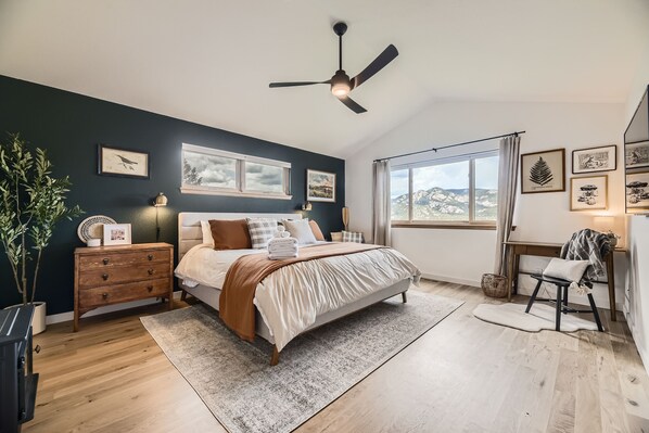 Quarto com cama, mesa de cabeceira, cômoda, ventilador de teto e janela com vista.