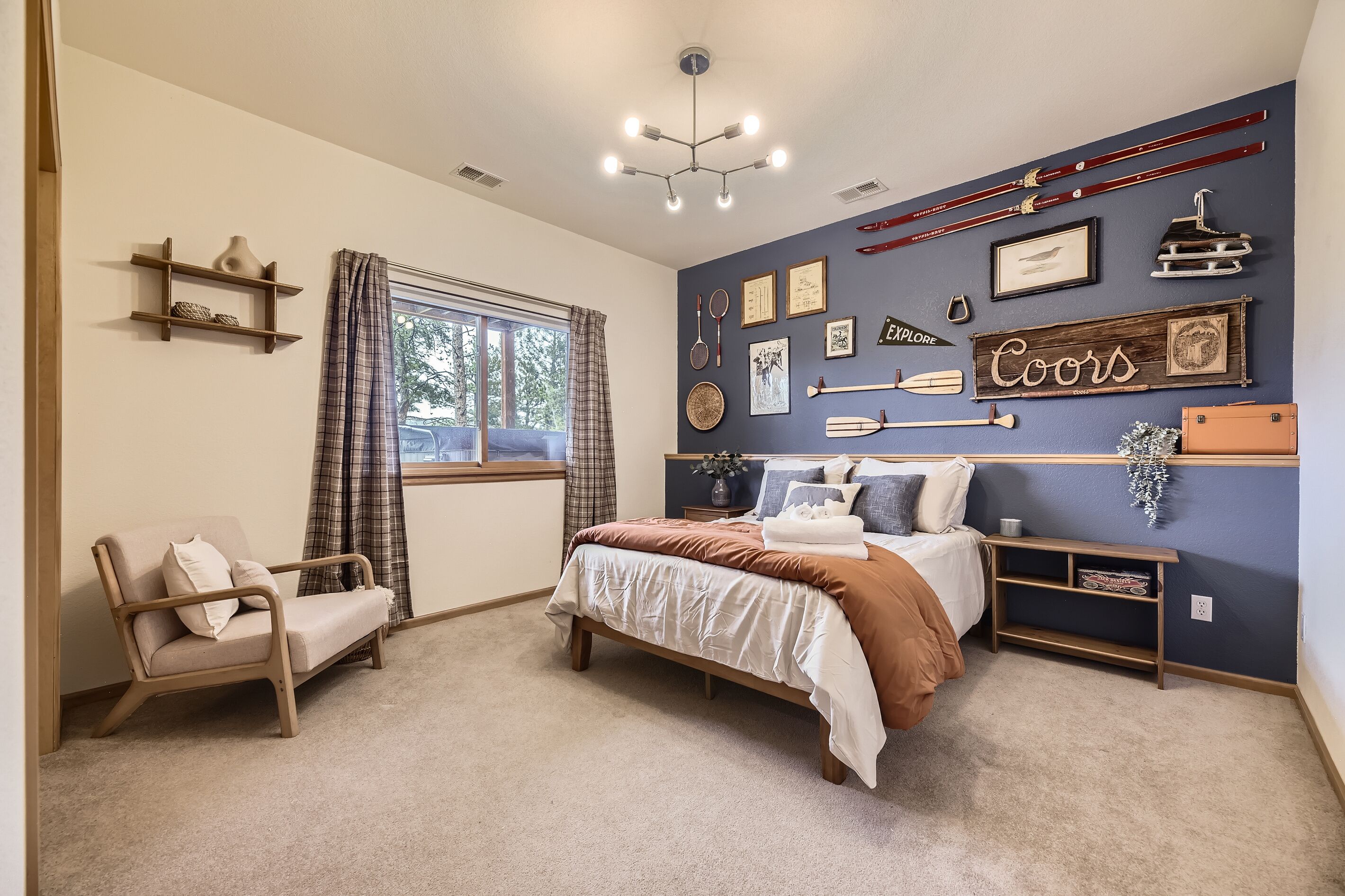 A bedroom with a bed, a chair, a window with curtains, a wall with various decorations, and a ceiling light.