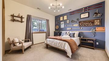 A bedroom with a bed, a chair, a window with curtains, a wall with various decorations, and a ceiling light.