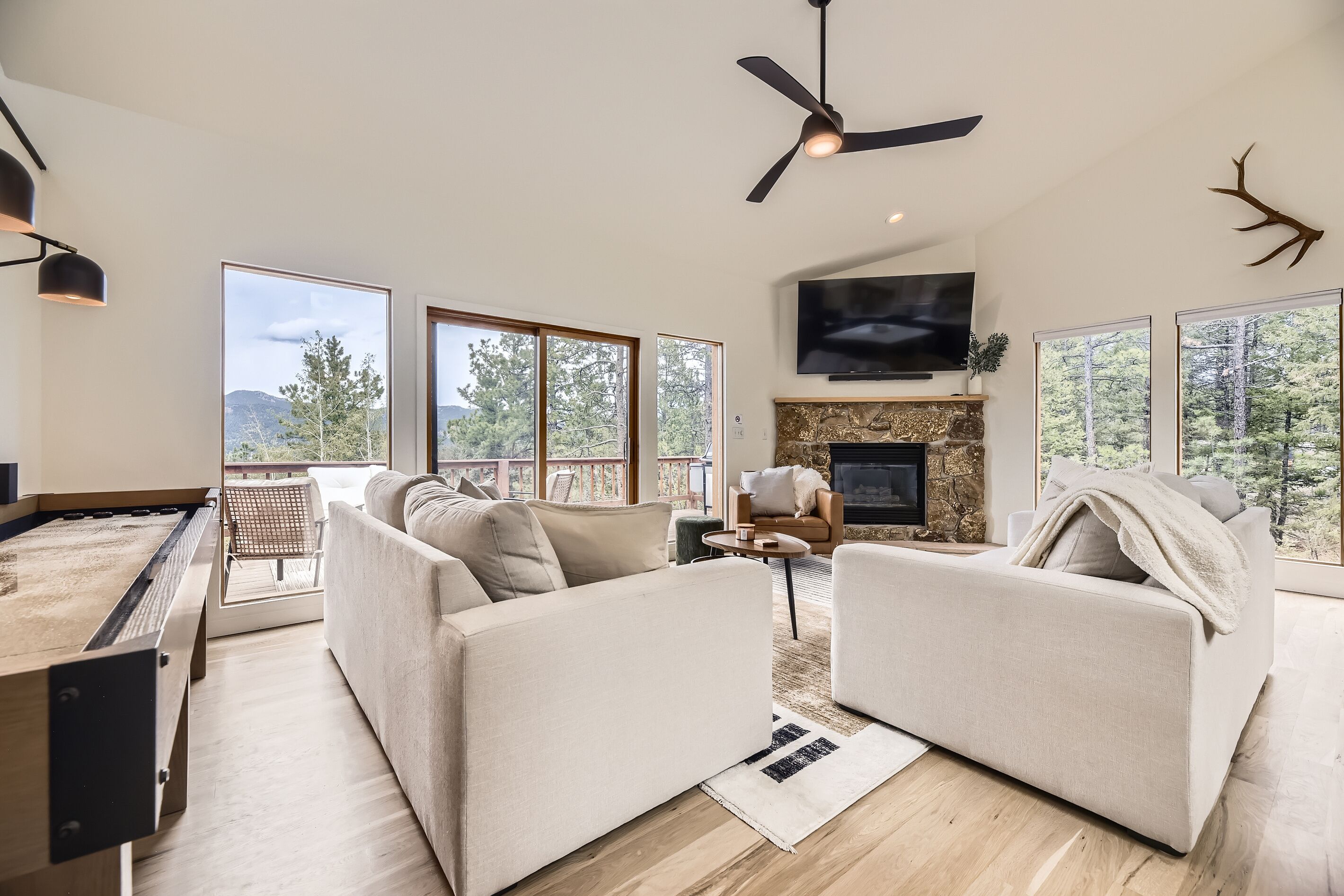 A modern living room with a fireplace, large windows, and a ceiling fan.