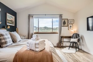 Quarto com cama, janela com vista para montanhas e mesa de cabeceira com abajur.