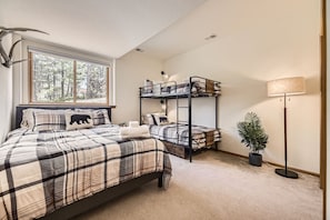 A bedroom with a bed, a bunk bed, a window with a forest view, a floor lamp, and a potted plant. - Serene Pine Foothills Cabin • Hot Tub & Deck Views (Pine)