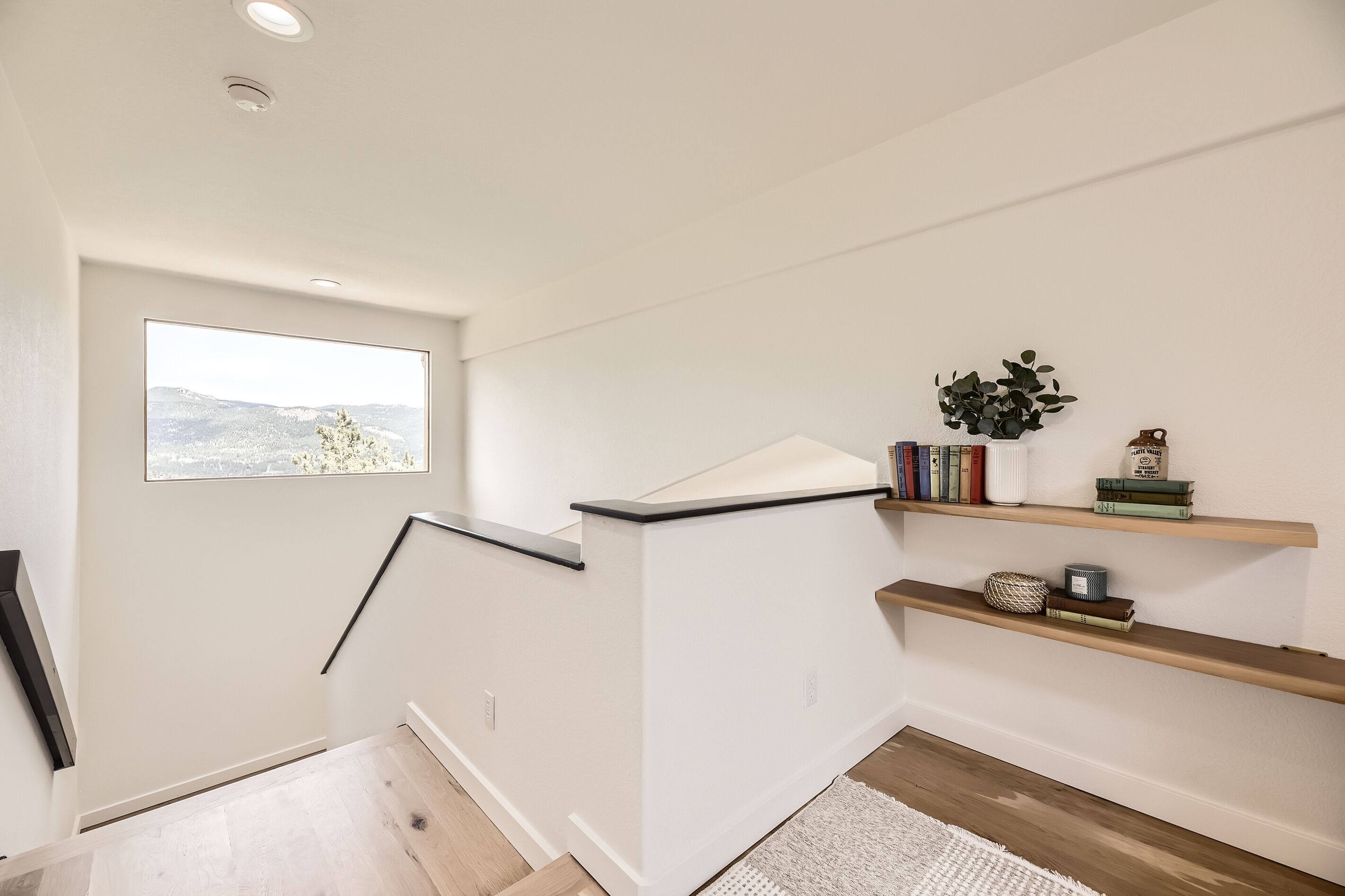 Una escalera moderna con barandilla negra, un ventanal con vista a un paisaje nevado, y una pared con estanterías llenas de libros y objetos decorativos.
