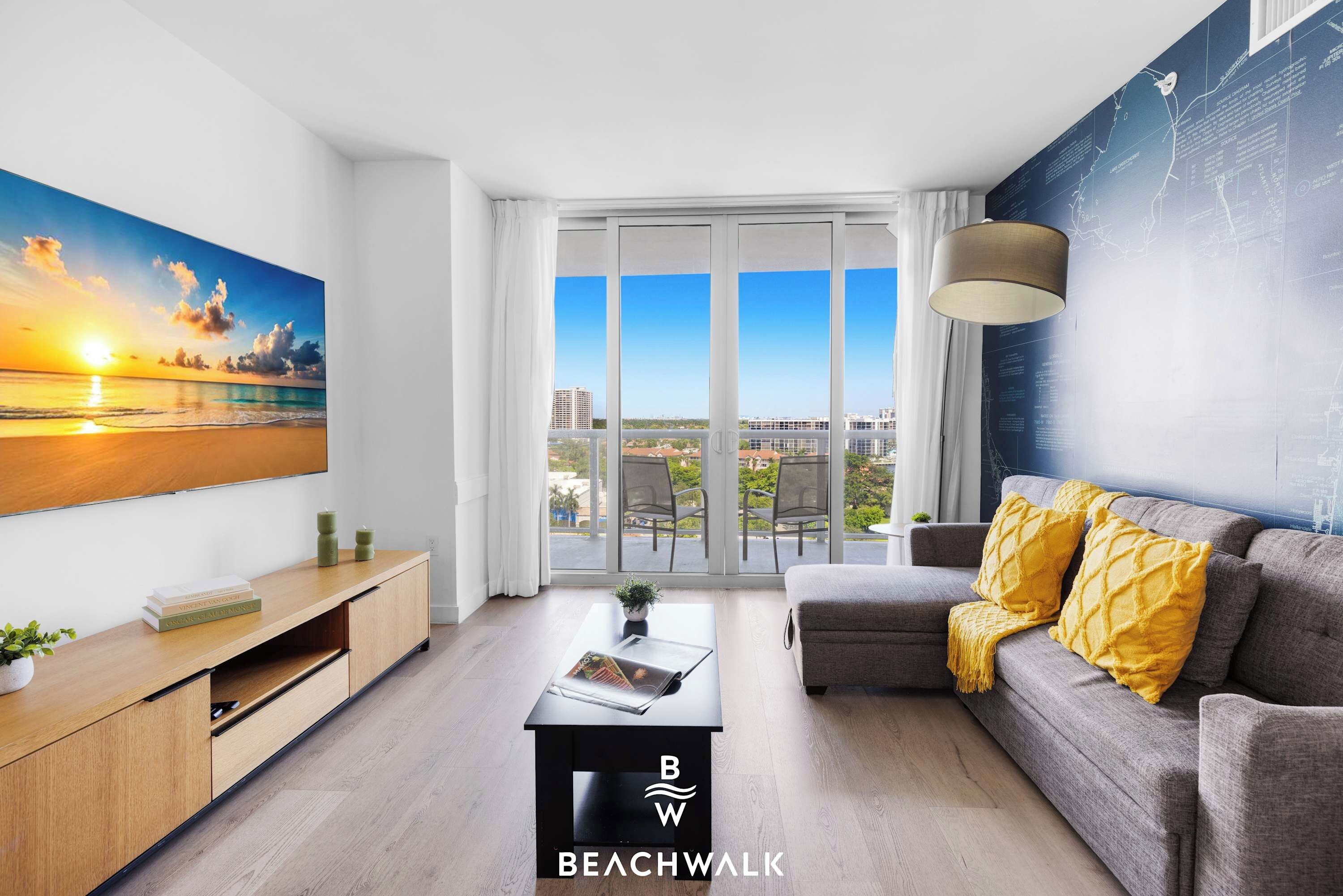 A modern living room with a large window, a sofa, a coffee table, and a painting of a sunset.