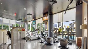 Academia com máquinas de cardio, aparelhos de musculação e uma grande janela com vista para a cidade.