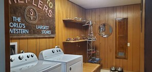 A laundry room with a wooden wall, a sign, a washing machine, a dryer, and shelves with toys. - Enjoy Longhorns at Texas Ranch House near Canyon Lake & Gruene – Sleeps 12 (New Braunfels)