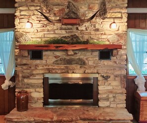 A stone fireplace with a metal firebox, a decorative shelf above, and a window with curtains on either side.