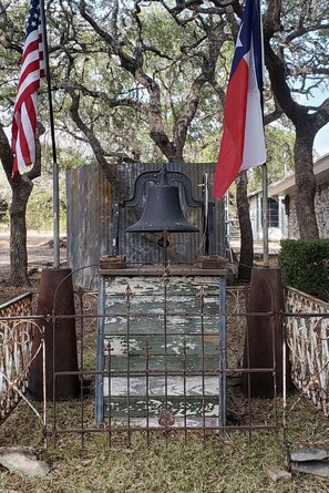A bell tower with two flags, surrounded by a metal fence and trees. - Enjoy Longhorns at Texas Ranch House near Canyon Lake & Gruene – Sleeps 12 (New Braunfels)