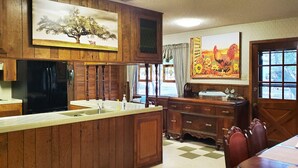 A kitchen with wooden cabinets, a refrigerator, a sink, and a dining area with a table and chairs. - Enjoy Longhorns at Texas Ranch House near Canyon Lake & Gruene – Sleeps 12 (New Braunfels)