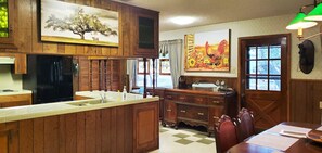A kitchen with wooden cabinets, a refrigerator, a sink, and a dining area with a table and chairs. - Enjoy Longhorns at Texas Ranch House near Canyon Lake & Gruene – Sleeps 12 (New Braunfels)