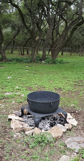 A campfire with a black pot on top, surrounded by rocks and greenery. - Enjoy Longhorns at Texas Ranch House near Canyon Lake & Gruene – Sleeps 12 (New Braunfels)
