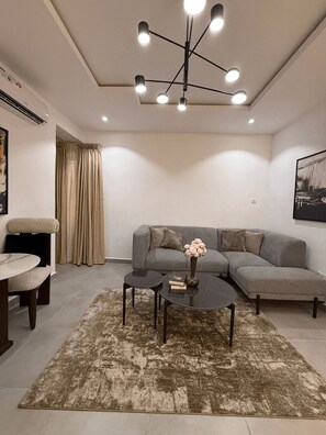 A modern living room with a grey sectional sofa, a round coffee table, and a contemporary chandelier. - Perfect 1-Bedroom in Victoria Island with Pool, Fast Wi-Fi & 24/7 Power (Lagos)