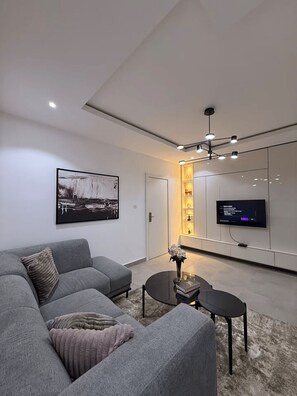 Un salon moderne avec un canapé gris, une table basse, un téléviseur à écran plat fixé au mur et un tableau accroché au mur.
