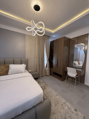 A modern bedroom with a large bed, a bedside table, a chair, a mirror, and a unique ceiling light fixture. - Perfect 1-Bedroom in Victoria Island with Pool, Fast Wi-Fi & 24/7 Power (Lagos)