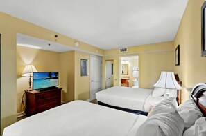 A hotel room with two beds, a TV, a desk, a lamp, and a bathroom visible through an open door. - Carolinian Resort  Ocean View Condo (Myrtle Beach)
