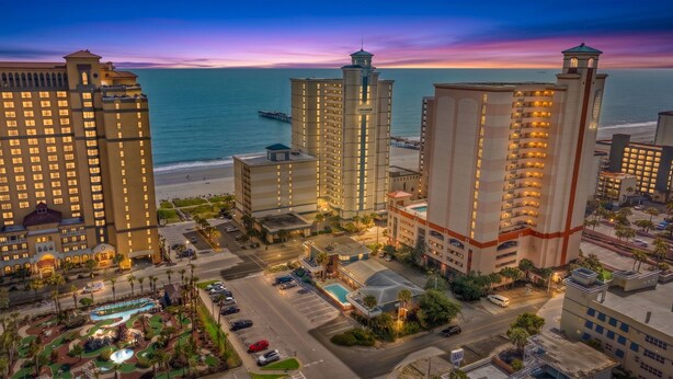 A hotel complex with multiple high-rise buildings, a beachfront, and a swimming pool area. - Carolinian Resort  Ocean View Condo (Myrtle Beach)