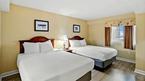 A hotel room with two beds, a nightstand with a lamp, and two framed pictures on the wall. - Carolinian Resort  Ocean View Condo (Myrtle Beach)