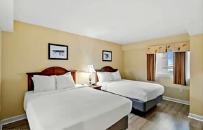 A hotel room with two beds, a nightstand with a lamp, and two framed pictures on the wall. - Carolinian Resort  Ocean View Condo (Myrtle Beach)