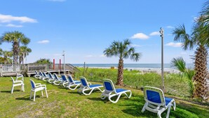 A beachside area with rows of sun loungers, palm trees, and a view of the ocean. - Carolinian Resort  Ocean View Condo (Myrtle Beach)
