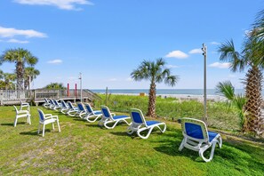 A beachside area with rows of sun loungers, palm trees, and a view of the ocean. - Carolinian Resort  Ocean View Condo (Myrtle Beach)