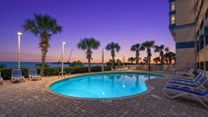 A swimming pool with lounge chairs and palm trees, surrounded by a brick patio. - Carolinian Resort  Ocean View Condo (Myrtle Beach)