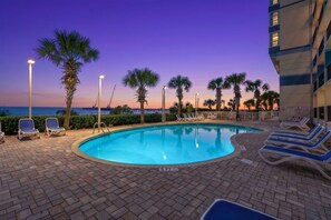A swimming pool with lounge chairs and palm trees, surrounded by a brick patio. - Carolinian Resort  Ocean View Condo (Myrtle Beach)