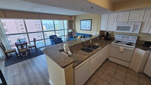 A kitchen with a granite countertop, stainless steel sink, white cabinets, and a white stove. - Carolinian Resort  Ocean View Condo (Myrtle Beach)